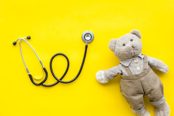 Wall Mural - Children's doctor concept. Teddy bear toy and stethoscope on yellow background top view copy space