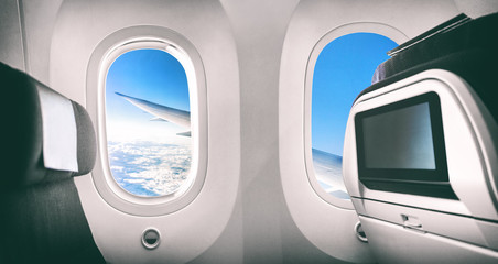 Airplane passenger seat plane interior with window view of flying aircraft wing and movie screen.