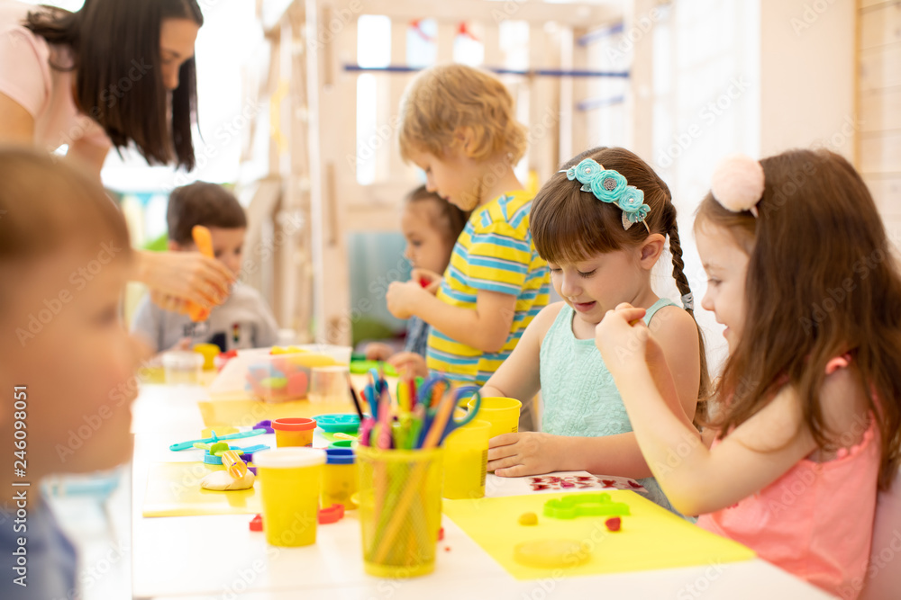Group of kindergarten children play with plasticine or dough. Little kids have a fun together with colorful modeling clay at daycare. - obrazy, fototapety, plakaty 