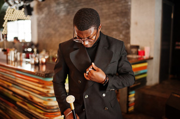 Stylish african american gentleman in elegant black jacket and glasses, holding retro walking stick as cane flask or tippling cane with golden diamond ball handle. Rich fashionable afro man.