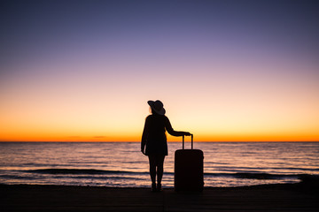 Relax woman with suitcase on a beach at sunset silhouette. Holiday travel concept. Young lady with suitcase on ocean landscape background