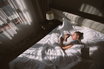 Top view - a young man is sleeping in his bed under the rays of the morning sun. The concept of early awakening and good mood for the whole day