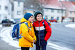 © Irina Schmidt - Two little kids boys of elementary class walking to school during snowfall. Happy children having fun and playing with first snow. Siblings and best friends with backpack in colorful winter clothes.