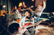 © chika_milan - Girls playing jazz music. In foreground one woman playing bass guitar and in background other three playing acoustic guitar, saxophone and drums. Home studio interior.