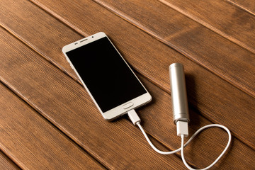 Silver power bank charging smartphone on wooden table