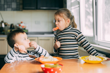 Wall Mural - Children eat pasta and sausage in the kitchen