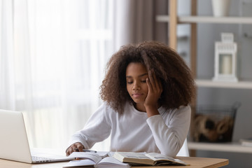 Wall Mural - Dreamy African American teenage girl sit at table with laptop and textbooks, distracted from doing homework, black teenager dream or think when preparing housework with handbook and notebook