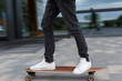 © Denis Mamin - Cropped shot of young man in black jeans and white sneakers riding on longboard to the left in urban area, hurry on a date, photo in motion/ side view/ wooden longboard, moving fast, city center.