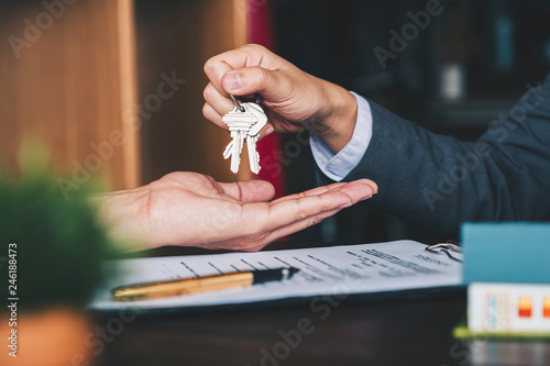 Fotografía estate agent giving house keys to woman and sign agreement in office