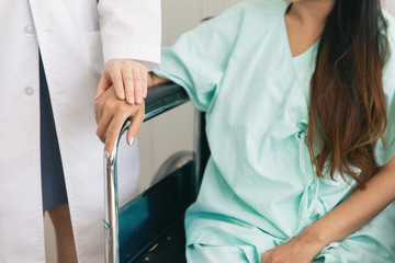 Woman doctor hold hand to reassuring female patient sitting on wheelchair in hospital room.