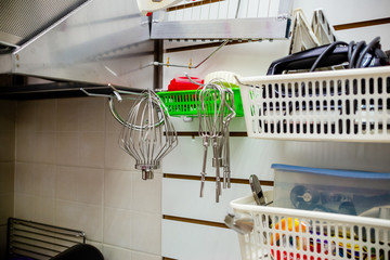 Set of metal kitchen utensils hanging on rack. Kitchen utensils hang on the shelf. Kitchen utensils hanging with steel hooks, white wall on background