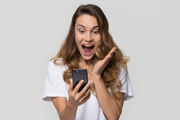 Excited young woman amazed by unbelievable shopping mobile app sale message looking at smartphone, euphoric girl winner holding cell phone screaming with joy isolated on white blank studio background