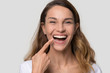 © fizkes - Happy young woman with white straight teeth perfect dent orthodontic smile pointing at tooth looking at camera isolated on studio blank background, dental health stomatology service concept, portrait