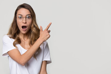 Wall Mural - Amazed girl student wear optic glasses pointing finger at copy space looking at camera isolated on white studio blank background, surprised woman customer show aside advertise product service sale