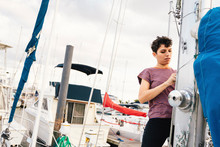 Woman Tying Sail On Mast While Standing Against Cloudy Sky In City