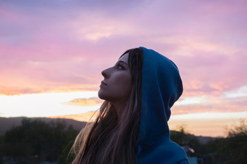 Young woman in the hood looks up at the evening sky