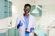 © sofiko14 - Black dentist in a dental clinic holds artificial jaws in his arm and shows a thumbs up