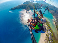 Paraglider Tandem Flying Over The Sea With Blue Water And Mountains In Bright Sunny Day. Aerial View Of Paraglider And Blue Lagoon In Oludeniz, Turkey. Extreme Sport. Landscape