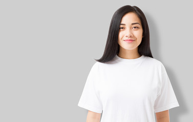 Wall Mural - Asian girl in blank template t shirt isolated on gray background. Young woman in tshirt copy space and mock up for advertising. White shirts. Front view.