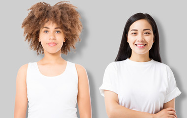 Wall Mural - Asian and african american girl in blank template t shirt isolated on gray background. Women in tshirt with copy space and mock up for advertising. White shirts. Front view