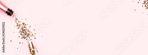 Golden confetti pouring from a bottle of champagne into a glass on pink backg...