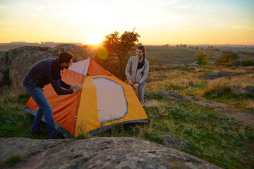Wall Mural - young couple assembling the tent at sunset in the mountains. adventure and family travel.