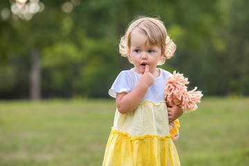 Sweet blond toddler girl with finger in mouth and knitted stuffed rag doll having fun walking outdoors