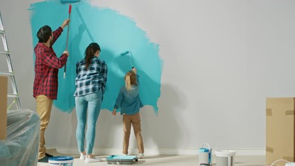 Wall Mural - Back Shot of a Young Family Painting Walls with Their Cute Small Daughter. They Paint with Rollers that are Covered in Light Blue Paint. Room Renovations at Home.