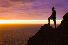 Visionary Man Standing On Top Of Cliff Edge Staring At Colorful Sunset By The Sea In Gran Canaria. Silhouette Of Person Witnessing Unique Twilight From Mountain Top. Successful, Entrepreneur Concepts