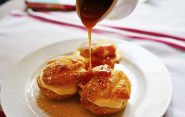 Wall Mural - Pouring hot caramel sauce over a profiterole, a French choux pastry filled with ice cream 