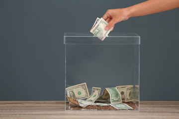 Sticker - Woman putting money into donation box on table against grey background, closeup