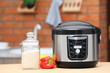 Modern electric multi cooker, jar of rice and peppers on table in kitchen