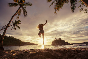 Wall Mural - Silhouette of female jump and enjoying on palm tropical beach on sunset