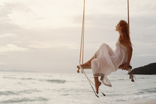 Silhouette Of Woman On Swing Above Sea Shore On Sunset