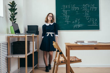 Wall Mural - Sad schoolgirl standing in front of blackboard.