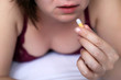 © Oleg - Sensual girl taking pill, young sexy woman in bra lies on the bed with capsule in hands. Concept of taking drugs, contraception, vitamin for beauty, slimming or sleeping pill