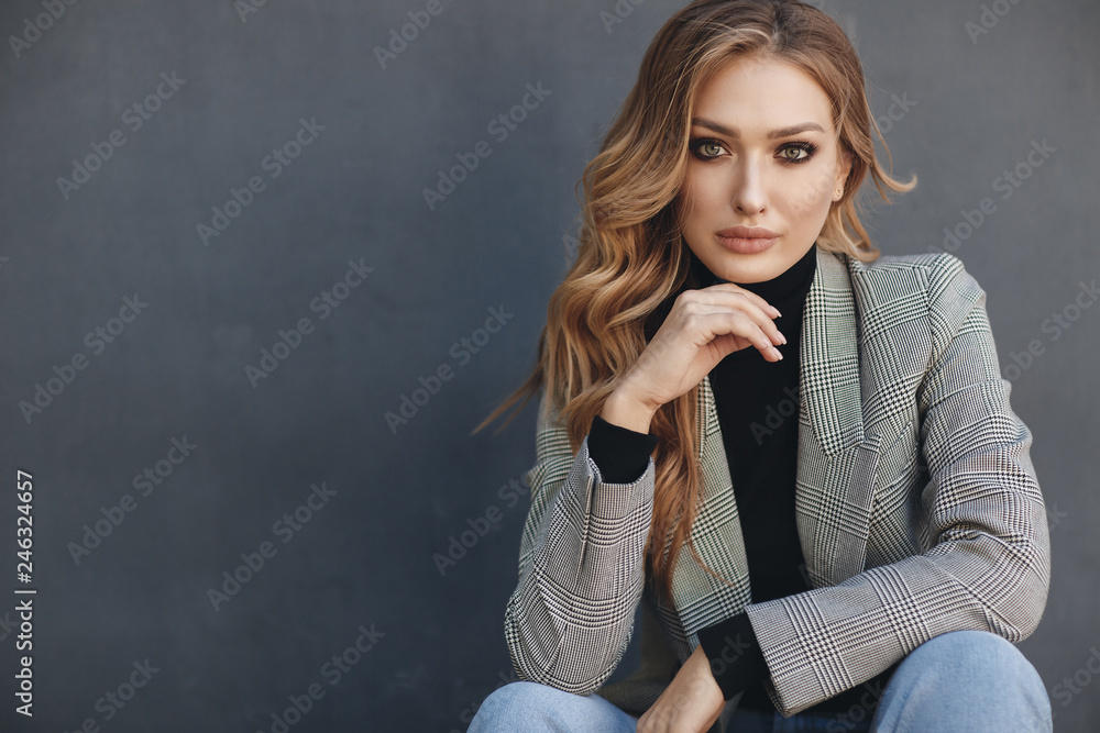Portrait of beautiful woman with long curly blond hair outdoors in spring. Young woman with natural makeup in a gray jacket . A smart photo of a young beautiful woman in autumn clothes. - obrazy, fototapety, plakaty 