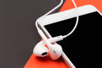 white earphones with phone on black  and red background.