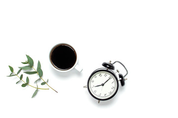 Flat lay cup of black coffee, black alarm clock, sprig of eucalyptus on white background top view copy space. Minimalistic food concept, morning breakfast, time to work, hot drink, coffee background