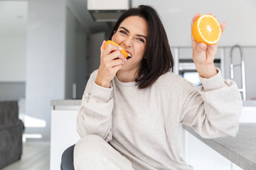 Wall Mural - Image of attractive woman 30s holding two pieces of orange, while sitting in living room