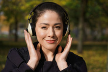 Young Woman In Her 20s Listening To Music With Cordless Over-ear Headphones Outside In Nature On A Sunny Day