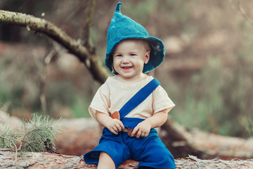 Outdoor pretty infant boy having fun outdoors in summer green forest in gnome's costume. Fun, childhood, nature concept