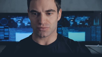 Portrait of developer programmer working on computer in a data center filled with monitor screens. Steadicam shot