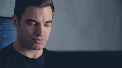 Portrait of developer programmer working on computer in a data center filled with monitor screens. Steadicam shot