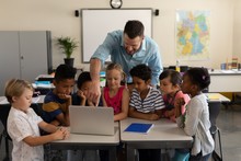 Male Teacher Teaching Kids On Laptop In Classroom