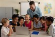© wavebreak3 - Male teacher teaching kids on laptop in classroom