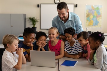 Wall Mural - Male teacher teaching kids on laptop in classroom