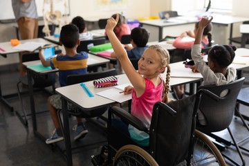 Wall Mural - Smiling disable schoolgirl looking at camera and raising hand in