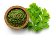 Dried chopped coriander leaves in a dark wood bowl next to fresh coriander leaves isolated on white from above.
