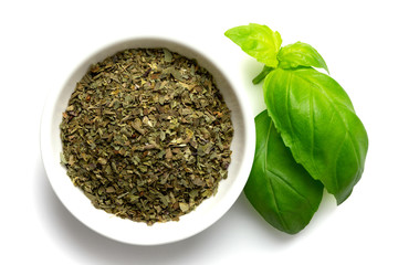 Wall Mural - Dried chopped basil in white ceramic bowl next to fresh basil leaves isolated on white from above.